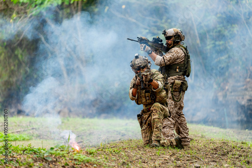 Militaries or soldiers stay in battlefield near the river with one sit down and one stand and point gun forward direction and in front of flare firework during outdoor practice.