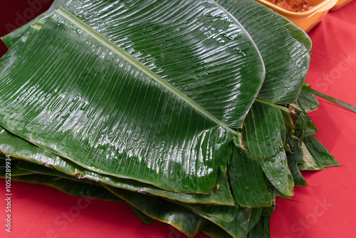 Washed banana leaves stacked together on a red table. photo