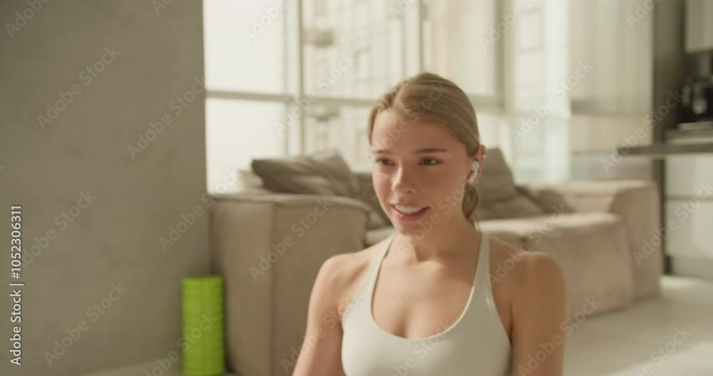 Woman celebrates workout success with a joyful smile and upbeat energy, holding wireless earbuds in a modern living room after a fitness session. Woman celebrates workout success with a joyful smile and upbeat energy, holding wireless earbuds in a modern living room after a fitness session.