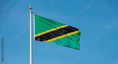 Tanzanian national flag waving on a flagpole against clear blue sky. photo