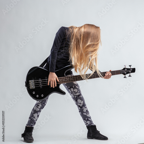Young blonde girl passionately playing electric bass guitar on w