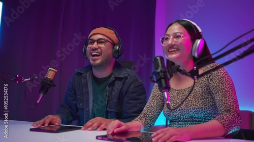 Two young asian streamer host making live podcast with condenser microphone and tablet at broadcast home studio. Content creator and social media influencer creating digital content.