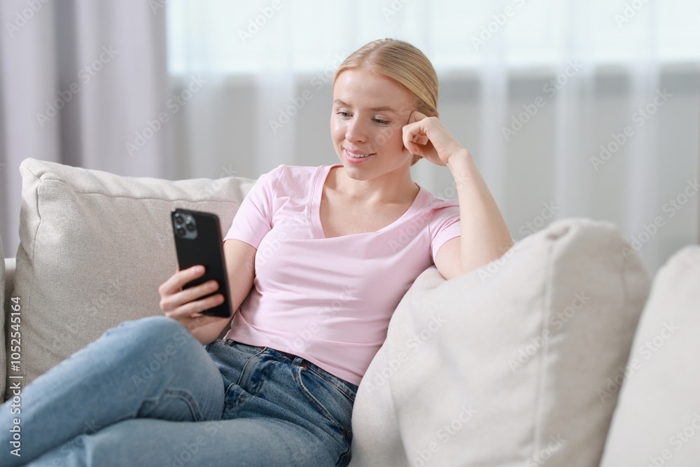 Smiling woman using smartphone on sofa indoors Smiling woman using smartphone on sofa indoors