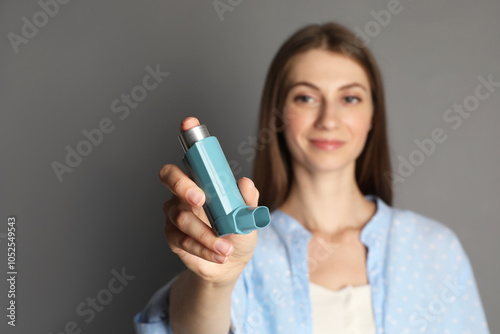 Young woman using asthma inhaler on grey background, selective focus photo