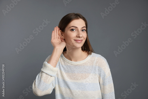 Woman showing hand to ear gesture on grey background photo