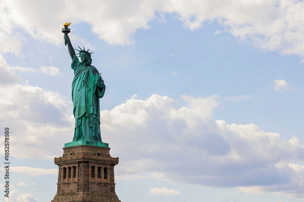 Obraz premium Iconic Statue of Liberty against a partly cloudy sky, symbolizing freedom and welcoming visitors to New York City.