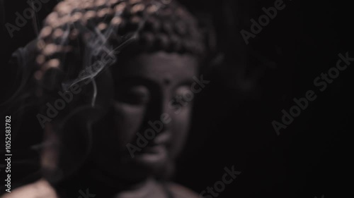 A smoldering incense stick in a holder, and a Tibetan singing bowl on a dark background next to the Buddha