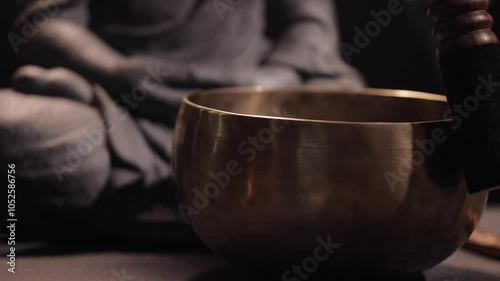 A smoldering incense stick in a holder, and a Tibetan singing bowl on a dark background next to the Buddha