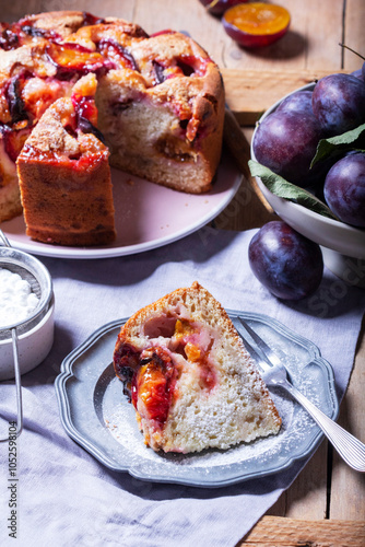 Obraz na płótnie Plum pie with filling and sugar crust, sprinkled with powdered sugar and plums on a wooden table. w salonie