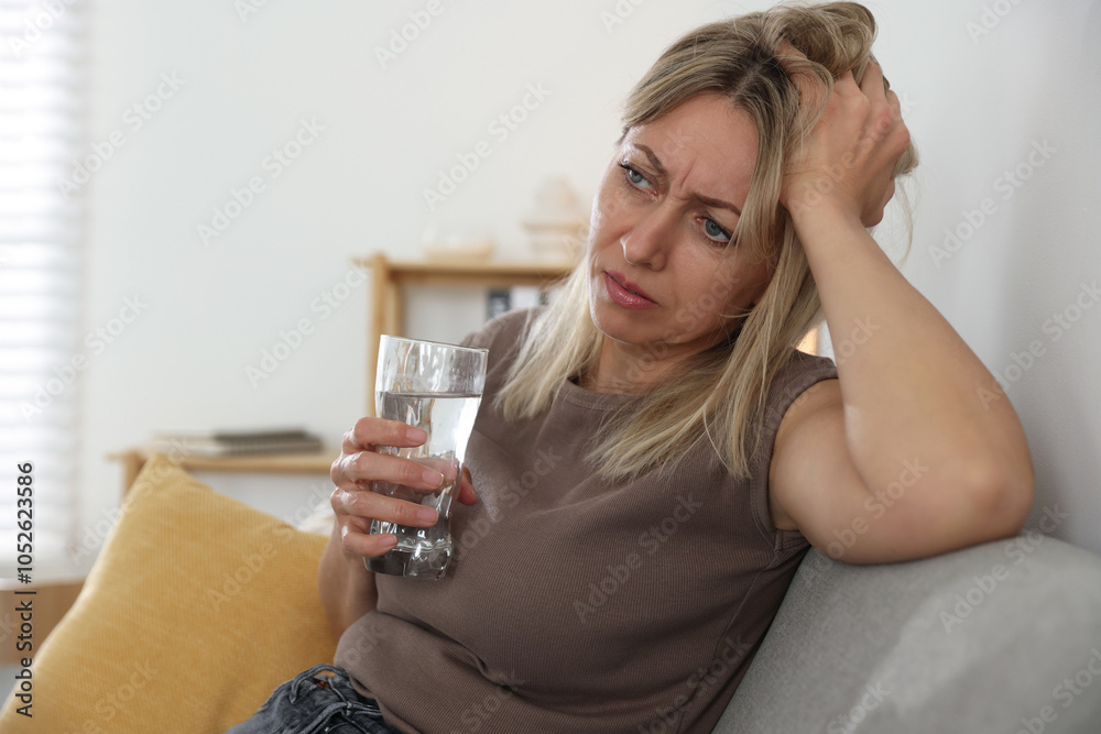 Menopause. Woman with glass of water suffering from headache on sofa at home Menopause. Woman with glass of water suffering from headache on sofa at home