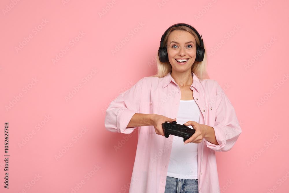 Happy woman in headphones playing video games with controller on pink background, space for text