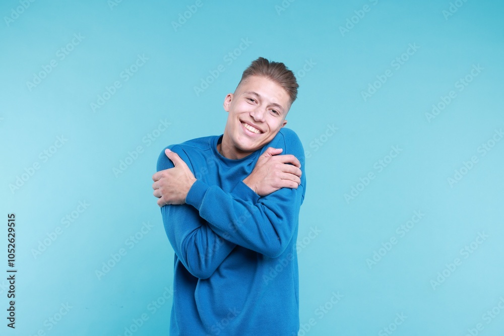 Young man hugging himself on light blue background Young man hugging himself on light blue background