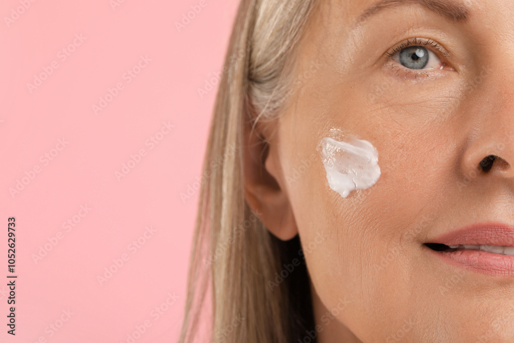 Senior woman with face cream on pink background, closeup. Space for text Senior woman with face cream on pink background, closeup. Space for text