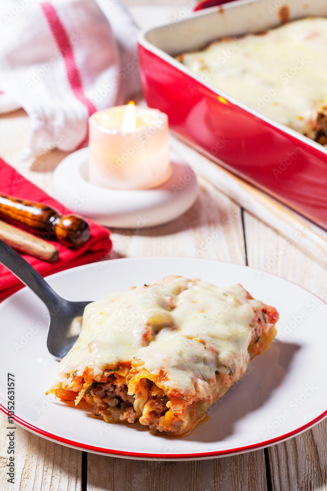 Cannellone with meat filling, tomato sauce and cheese on a light wooden table.