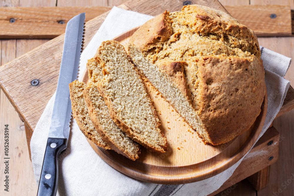 Homemade Irish soda bread cut into pieces and knife on wooden background.