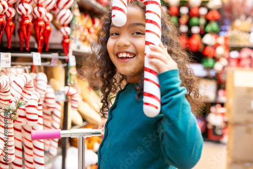 Smiling girl holding giant candy cane having fun christmas shopping