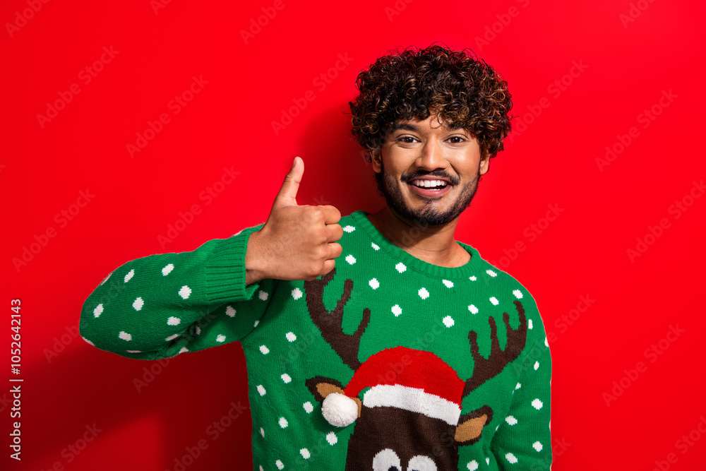 Photo of nice young man show thumb up wear christmas sweater isolated on red color background Photo of nice young man show thumb up wear christmas sweater isolated on red color background