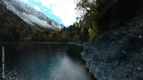 a magical high-altitude lake in the mountains of Abkhazia in autumn with beautiful trees and snowy mountains in the background, flying on a drone