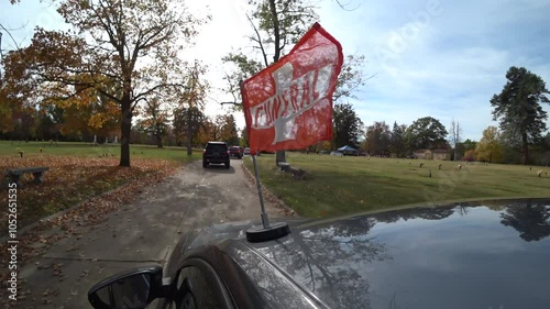 Orange funeral flag on car in procession approaching grave site.