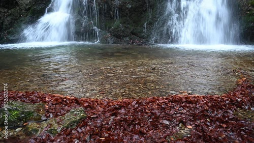 The pond of a twofold waterfall with autumn leaves in the foreground