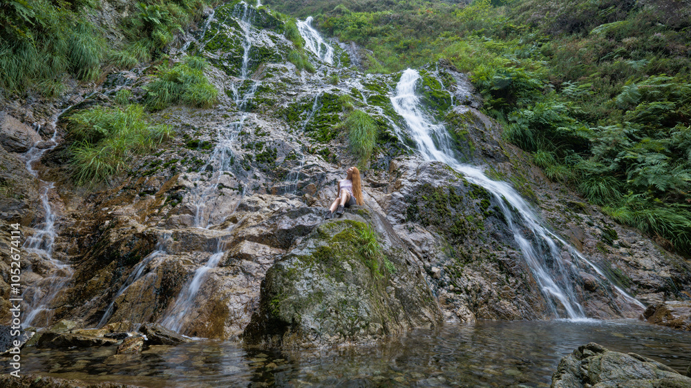 Obraz premium Cascading waterfall flows down a moss-covered rocky hillside.