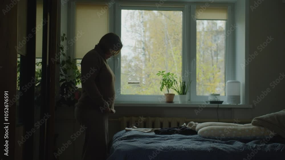 A pregnant woman standing in a room by the window puts on a sweater before a walk and strokes her belly
A pregnant woman standing in a room by the window puts on a sweater before a walk and strokes her belly