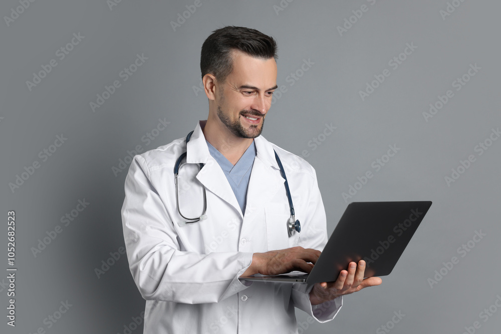 Smiling doctor with stethoscope and laptop on grey background Smiling doctor with stethoscope and laptop on grey background
