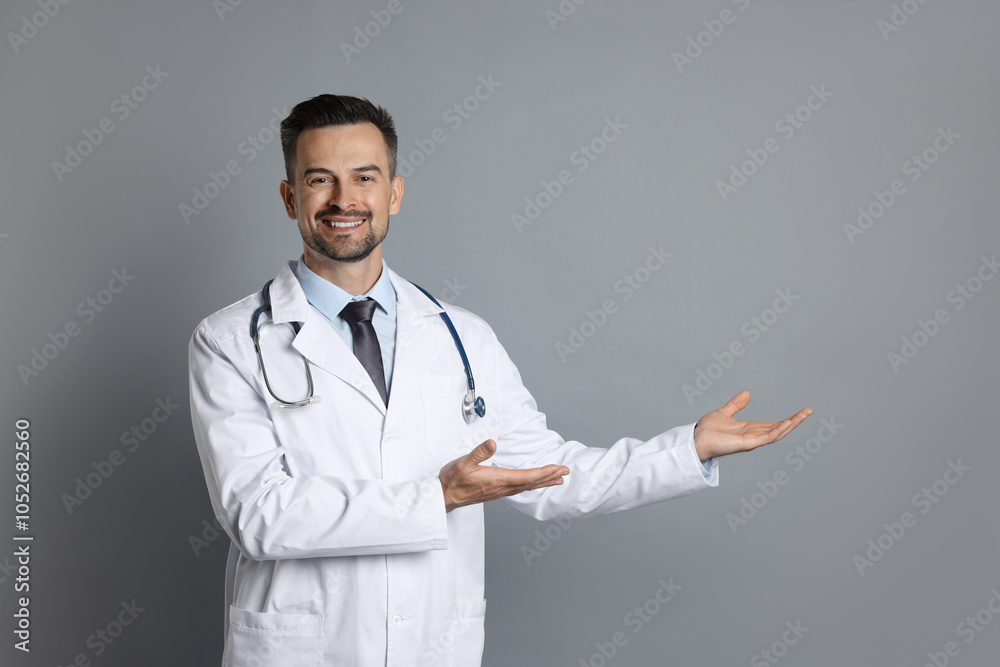Smiling doctor with stethoscope pointing at something on grey background Smiling doctor with stethoscope pointing at something on grey background