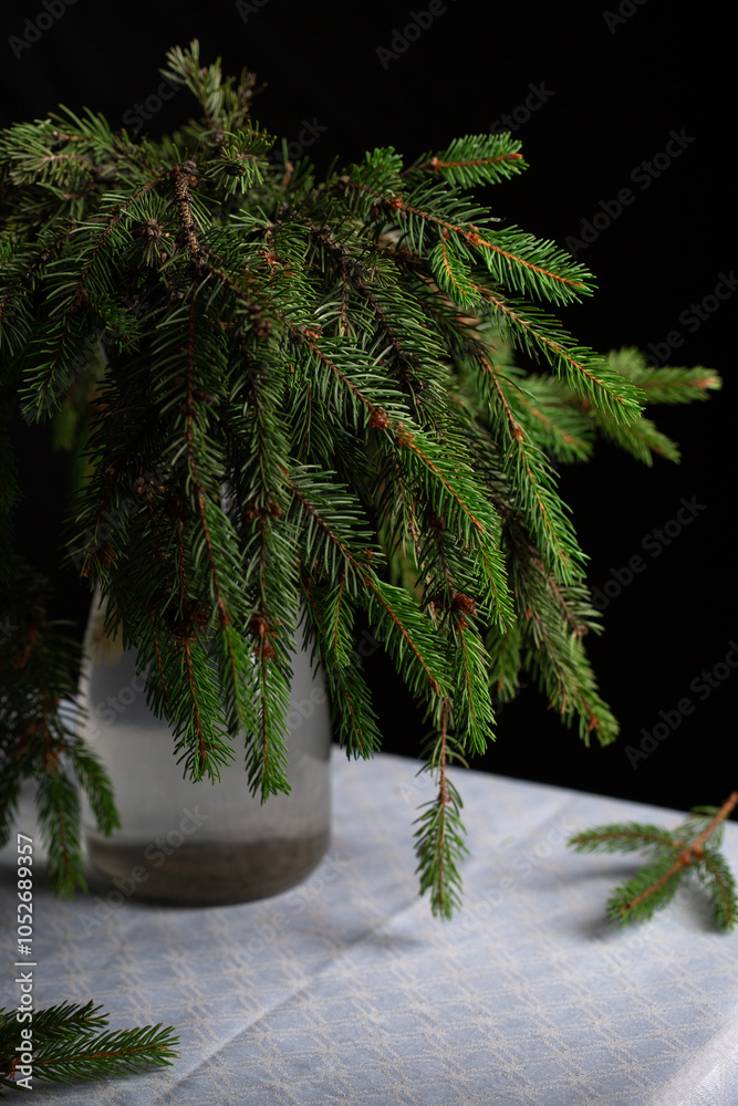 A transparent vase with green fluffy branches of a Christmas tree stands on the table