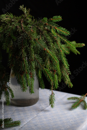A transparent vase with green fluffy branches of a Christmas tree stands on the table