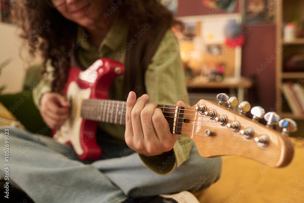Fototapeta premium Person sitting on couch while playing electric guitar, focusing on strumming technique to create music in a cozy indoor setting
