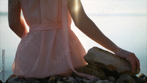 Cuadro en lienzo Woman relaxing on rocks by the sea at sunset touching stone