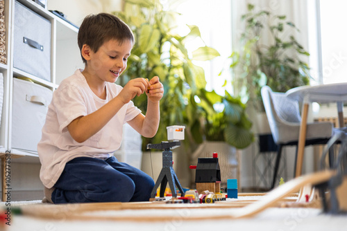 A small white-skinned European child builds a toy railway at home on the carpet. 