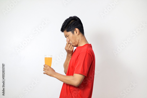 Asian man wearing red shirt who is reluctant to smell orange juice by covering his nose 
