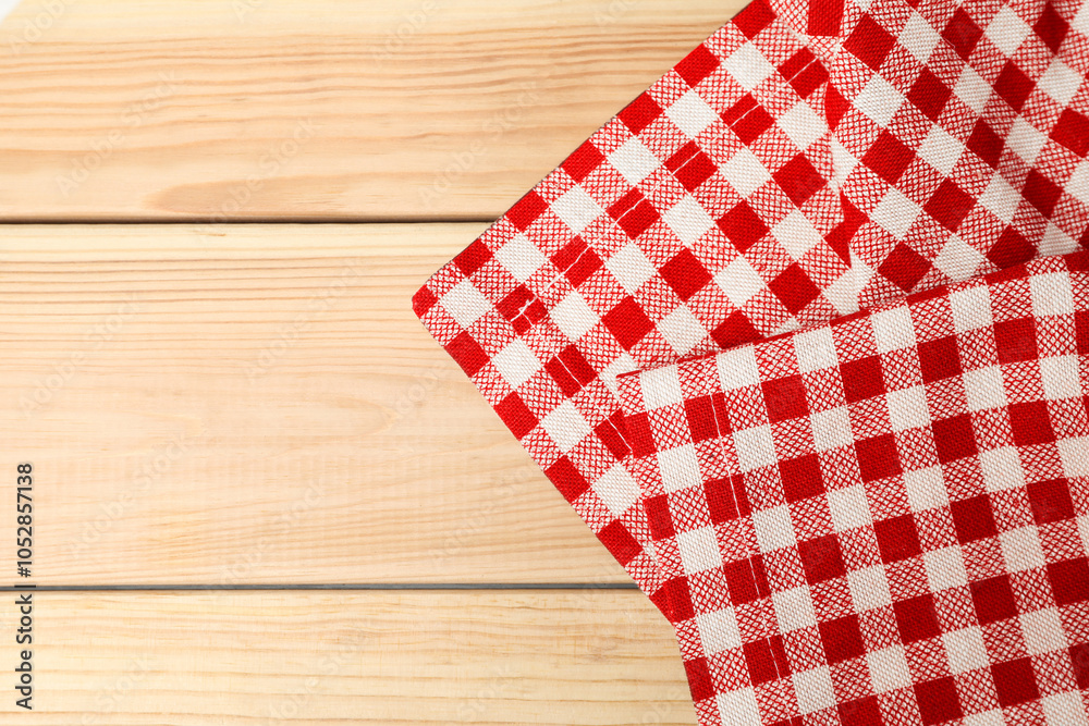 Obraz premium Folded tablecloth with checkered pattern on light wooden table, top view. Space for text