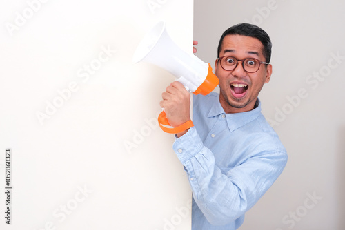 A man holding megaphone peeking behind a wall showing wow face expression photo