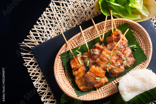 Thai street food concept Moo ping, Mu Ping, Thai-style grilled bbq pork skewers with rice stick on black background with copy space