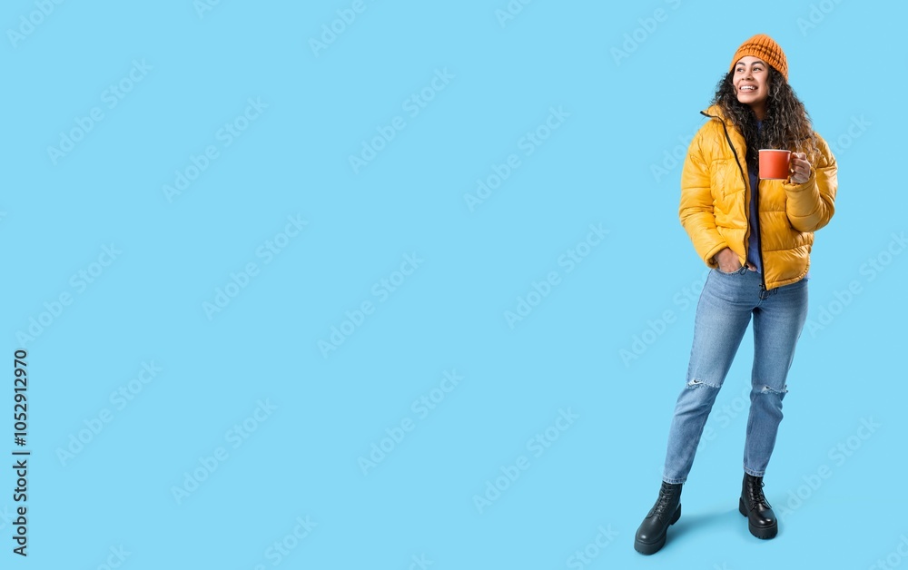 Fototapeta premium Happy young African-American woman with cup of hot mulled wine on blue background with space for text