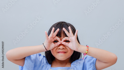 adorable Asian child seriously doing funny faces making with finger glasses shape like glasses looking through binoculars. isolated on light color background.