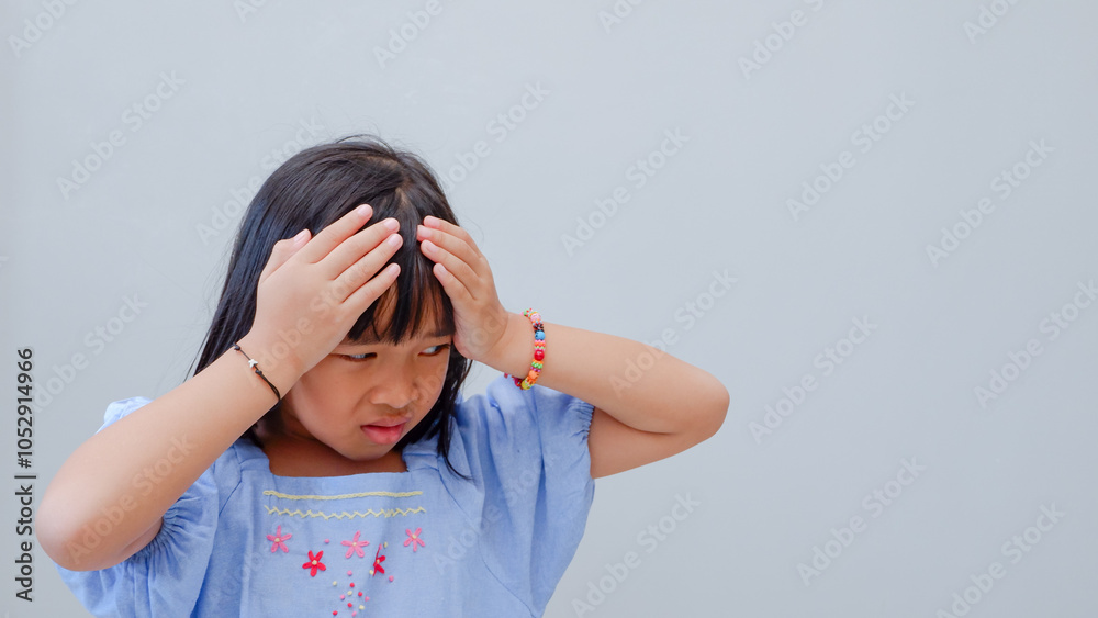 Frustrated cute Asian child girl wearing blue dress holding on forehead being depressed regretting what he did having headache, looking stressful. Frustrated cute Asian child girl wearing blue dress holding on forehead being depressed regretting what he did having headache, looking stressful.