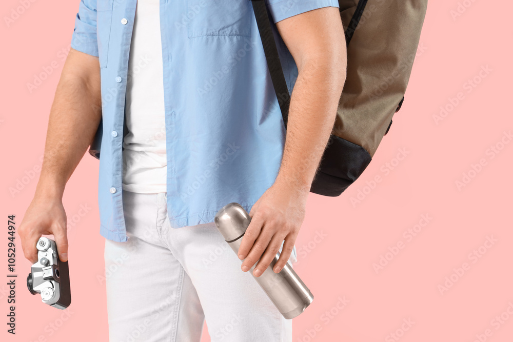 Male tourist with backpack, thermos and photo camera on pink background Male tourist with backpack, thermos and photo camera on pink background