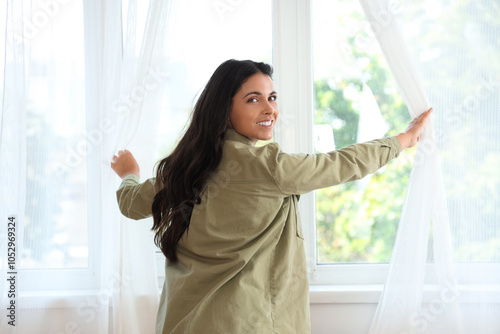 Beautiful woman opening curtains in room on moving day, back view