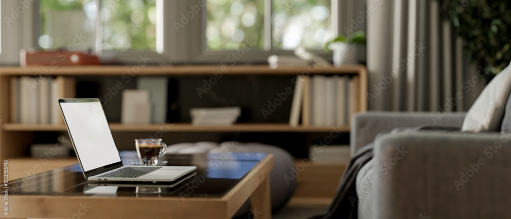A side view of a laptop and a coffee cup on a coffee table in a contemporary living room. A side view of a laptop and a coffee cup on a coffee table in a contemporary living room.