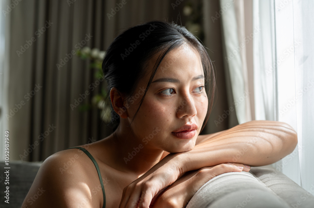 A beautiful, thoughtful woman is sitting on a sofa at home, looking out the window, deep in thought. A beautiful, thoughtful woman is sitting on a sofa at home, looking out the window, deep in thought.