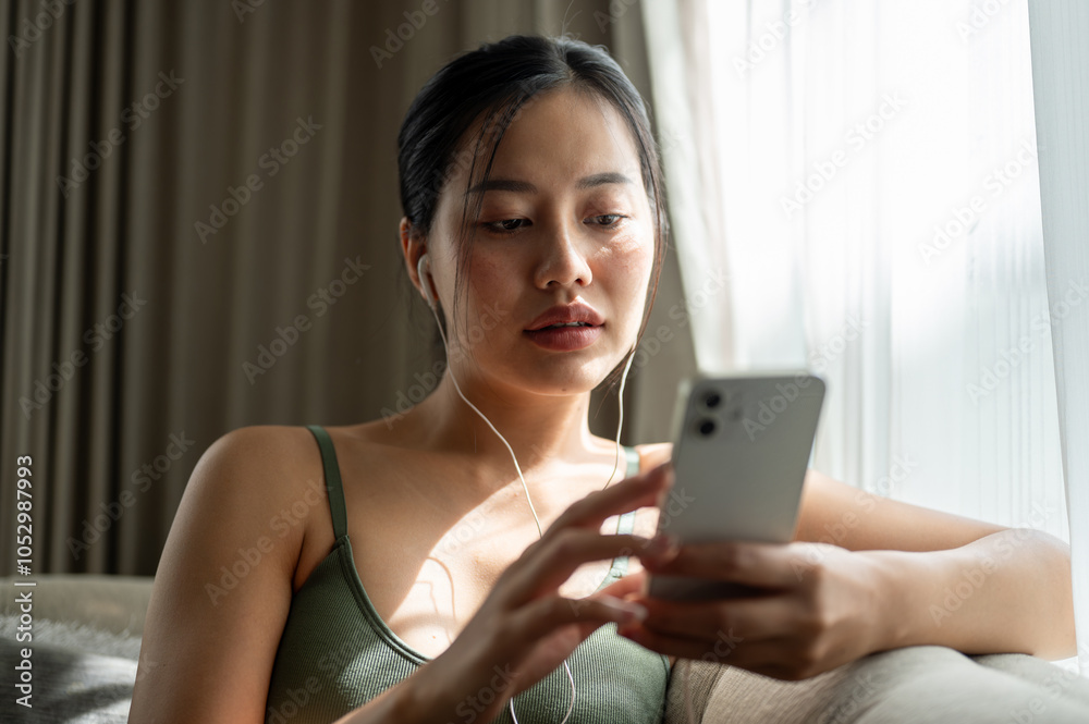 A beautiful woman reading chat on her phone while listening to music through her earphones on a sofa A beautiful woman reading chat on her phone while listening to music through her earphones on a sofa