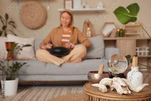 Sheep skull with crystal ball and Tibetan bowl on table against woman playing glucophone at home, closeup