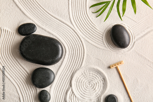 Photography Black stones and small rake on light sand with lines. Zen concept