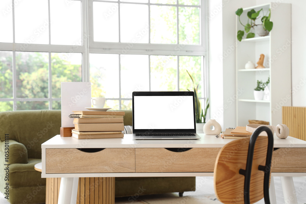 Blank laptop with books on programmer's desk in light living room Blank laptop with books on programmer's desk in light living room