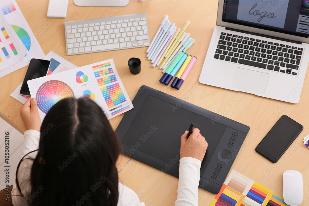 Young female graphic designer working with tablet and color palette at table in office Young female graphic designer working with tablet and color palette at table in office