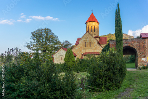 The main entrance to the Betania monastery. The main church in the rays of the setting sun. A tall cypress. A hill and sky in the background photo